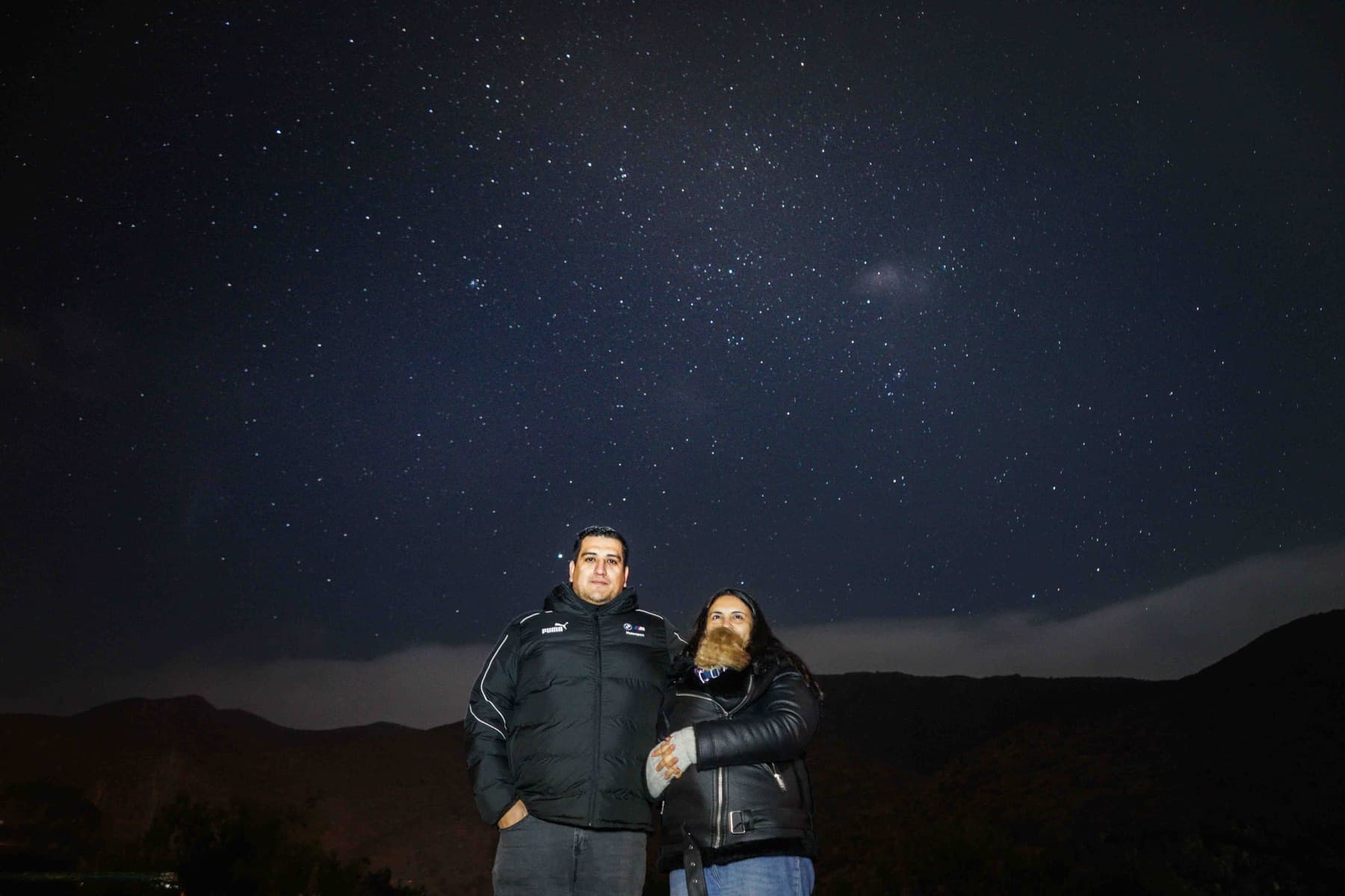 Una pareja posa de noche en el Molle bajo un cielo cubierto de estrellas.